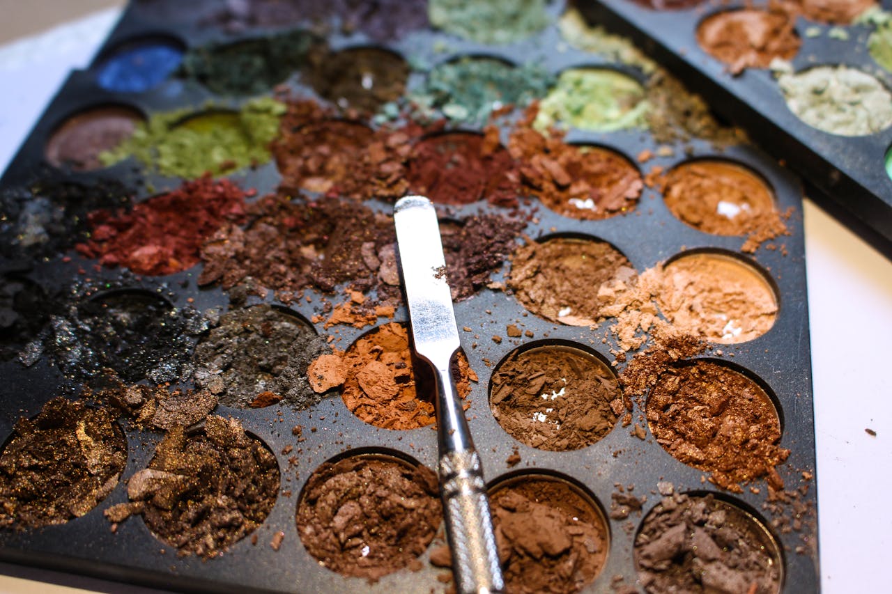 Close-up of a colorful, messy makeup palette with scattered eyeshadow powders.