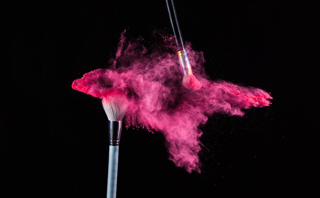 High-speed capture of makeup brushes dispersing vibrant pink powder on black background.